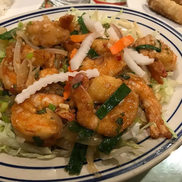 A close-up of Vietnamese shrimp with vegetables and sauce on a white plate with blue stripes.