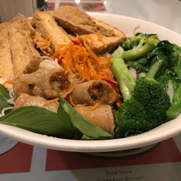 Vietnamese vermicelli bowl with fried tofu, spring rolls, shredded carrots, broccoli, and basil.