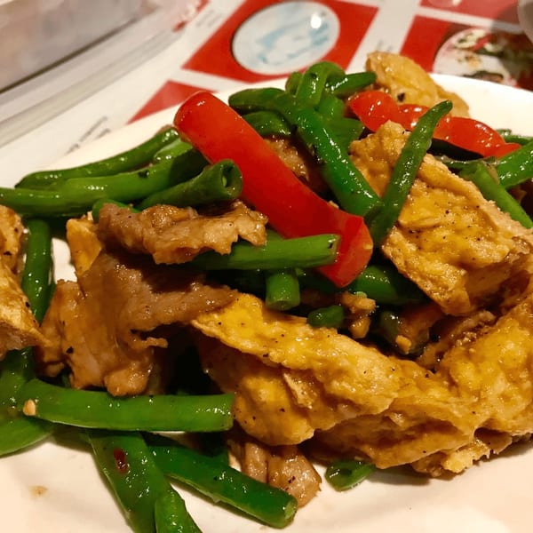 Vietnamese stir-fried green beans, red peppers, tofu, and meat on a white plate.