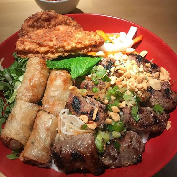 A vibrant Vietnamese vermicelli bowl with grilled meat, crispy spring rolls, and fried shrimp cake.