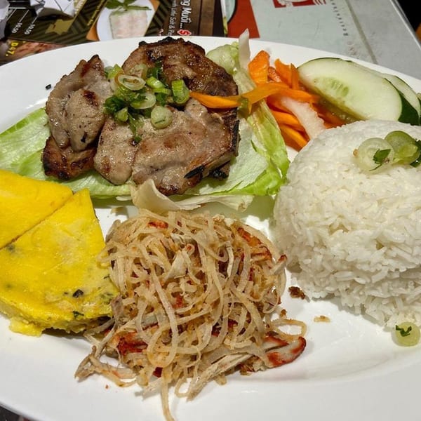 Vietnamese grilled pork with rice, egg cake, shredded pork skin, and pickled vegetables on a white plate.
